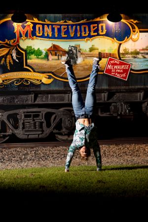 Person doing a handstand on grass in front of a vintage train car with colorful Montevideo artwork painted on its side.