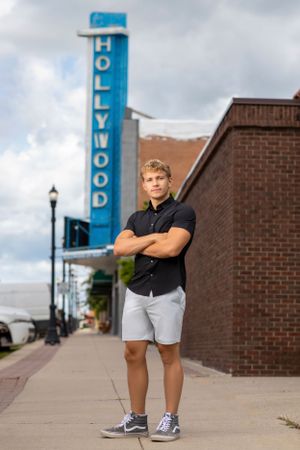Person posing near a brick building with a vintage Hollywood sign in the background on a cloudy day.