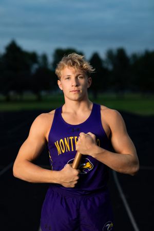 High school athlete in purple Montana team uniform poses on track at dusk.