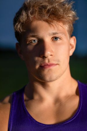Close-up outdoor portrait of someone wearing a purple tank top in warm evening lighting against a blue sky background.
