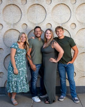 A group of four people posing together against a decorative wall with circular indentations.