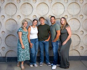 A group of five people stand together in front of a textured wall with circular patterns.