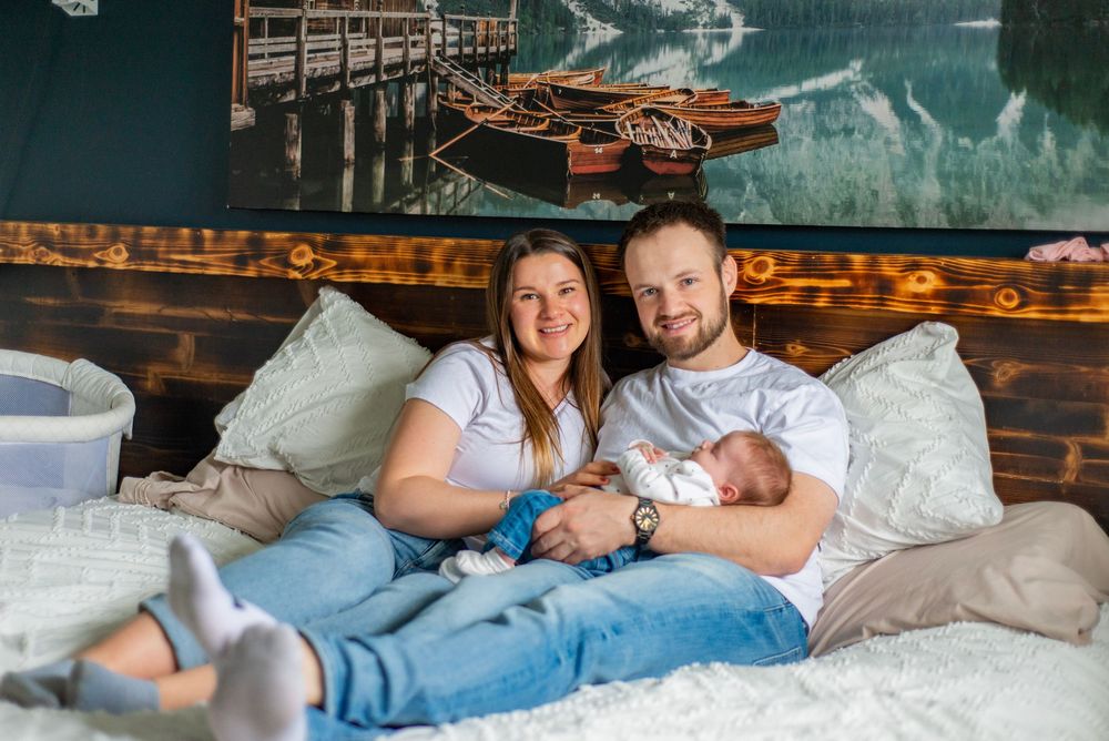 A couple relaxes on a bed with their newborn baby in a room decorated with nautical artwork and pillows.