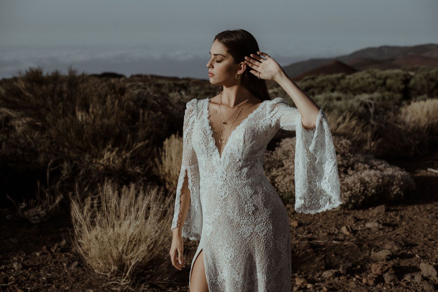 A delicate white lace wedding gown with bell sleeves stands out against a desert landscape.