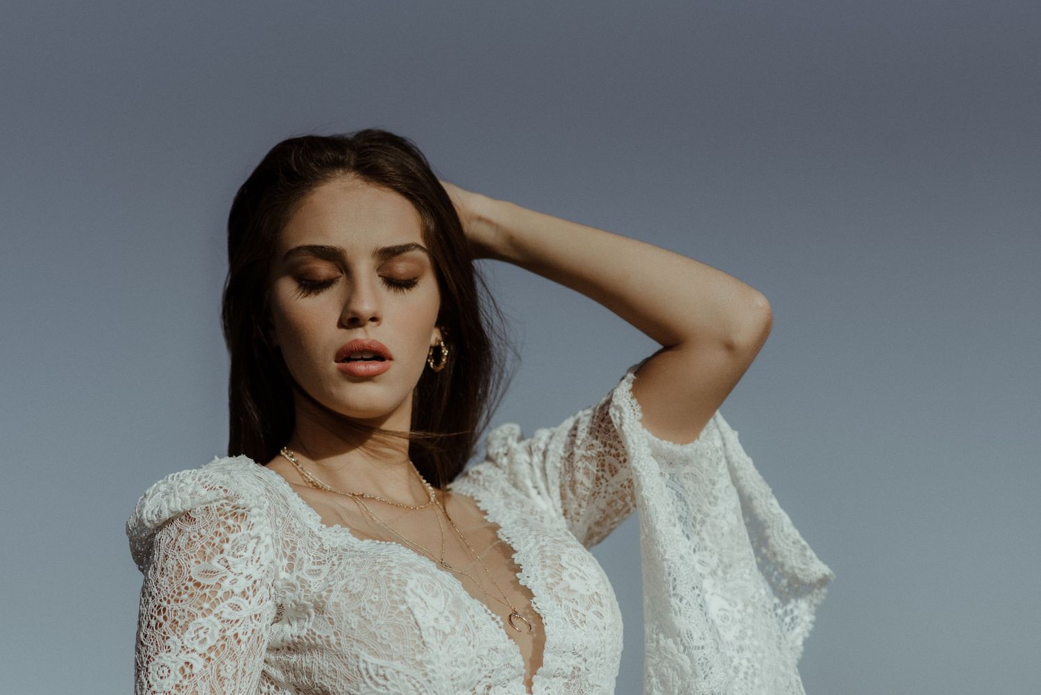 White lace wedding dress with dramatic sleeves photographed against a grey backdrop.