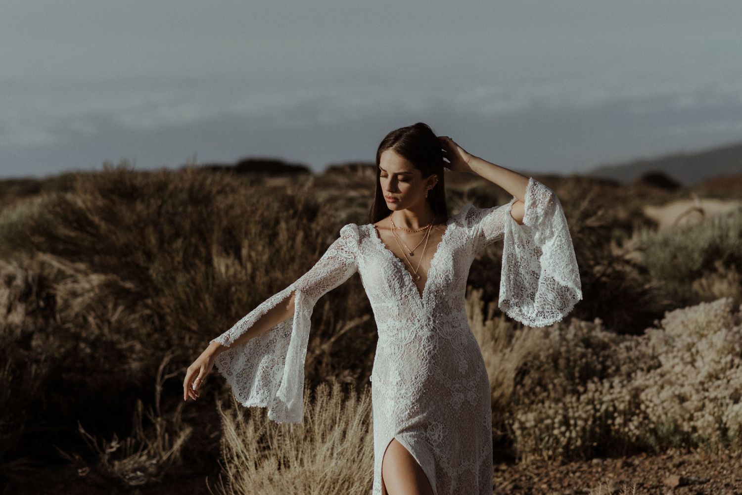 Flowing white wedding dress with bell sleeves captured in desert terrain.