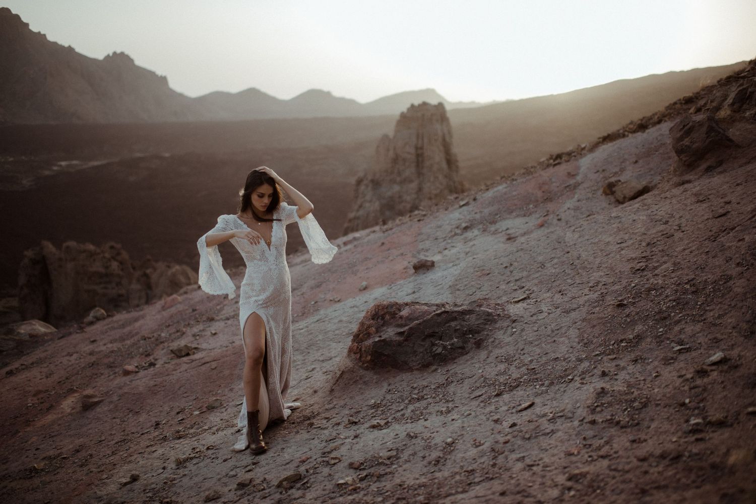 A dramatic fashion portrait in a white dress against a mountainous desert landscape at sunset.