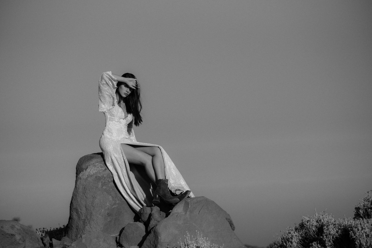 A silhouette poses artistically on a rock formation against a minimalist sky.
