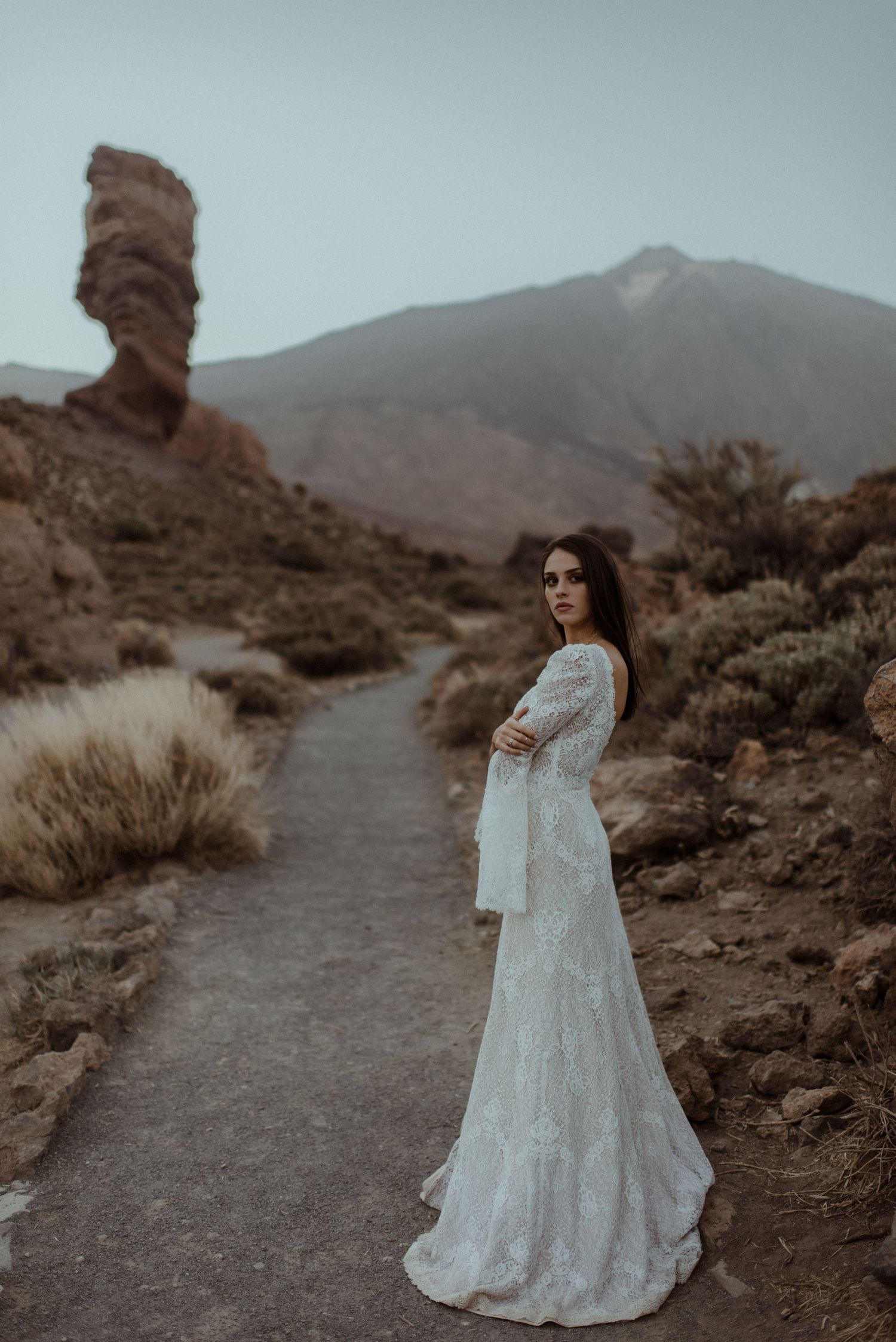 An elegant portrait featuring a lace wedding dress against a distinctive rock formation and mountain backdrop.