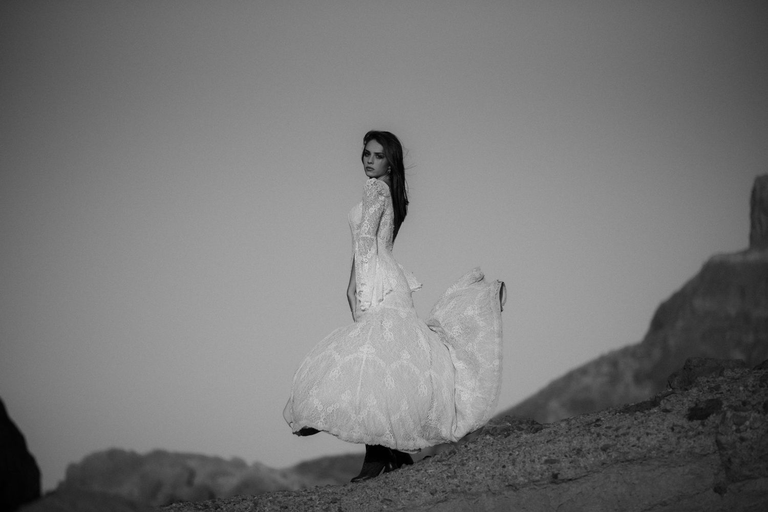 Black and white photograph of a bride in a flowing dress on a hillside.