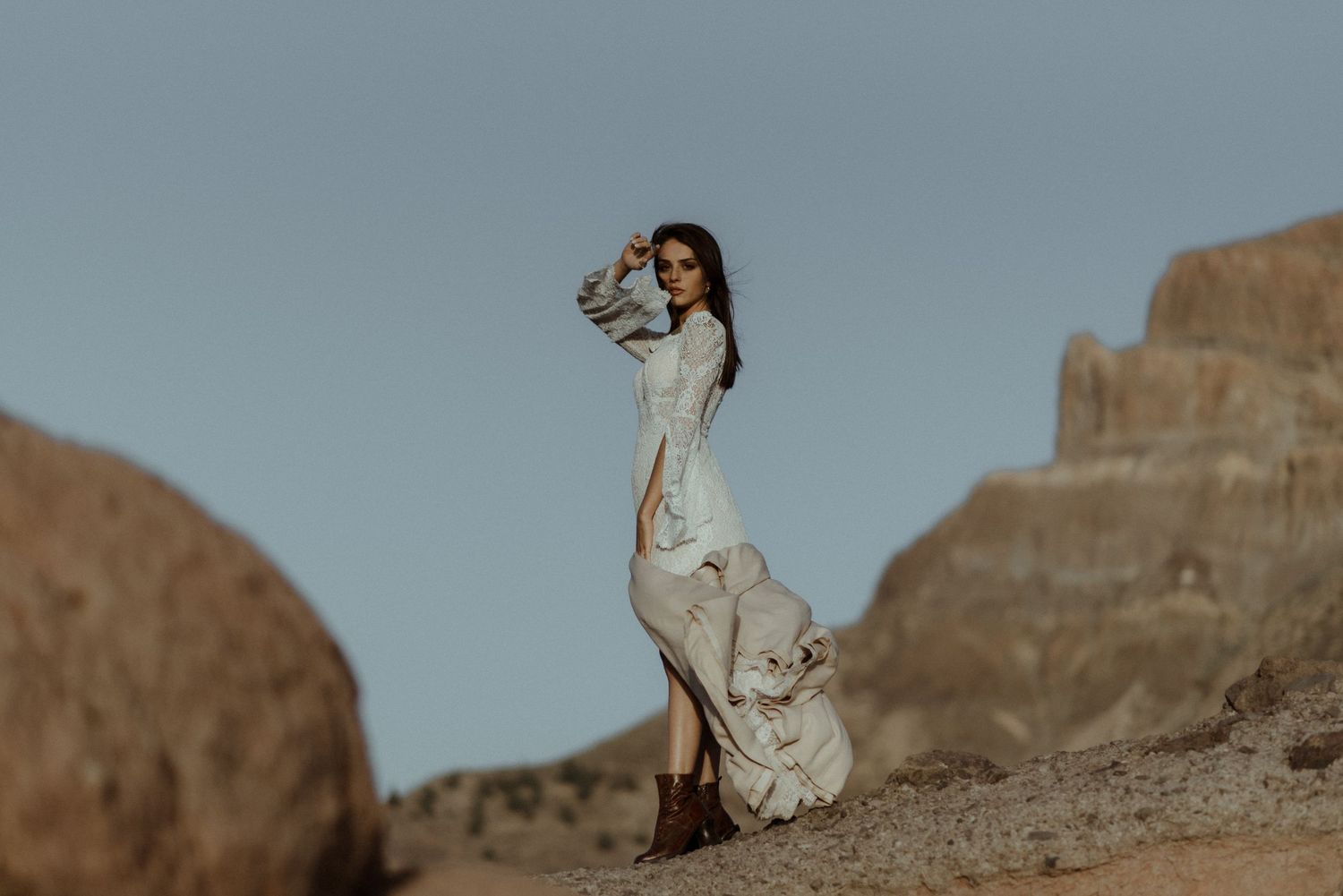 Dramatic bridal portrait on rocky terrain wearing a vintage-style lace dress.