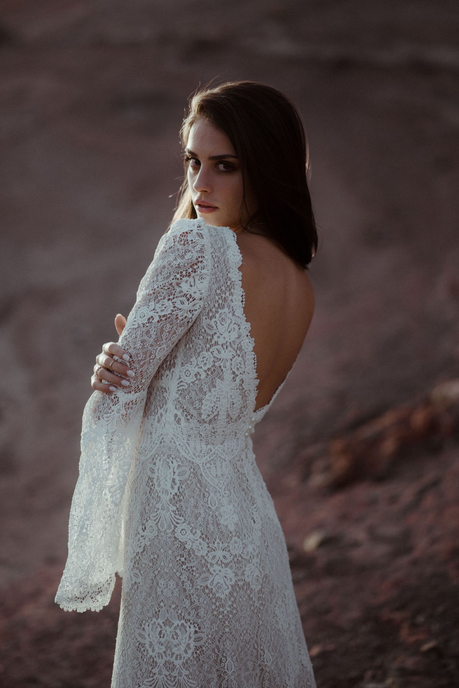 Elegant backlit portrait in a white lace wedding dress against rustic rock formations.
