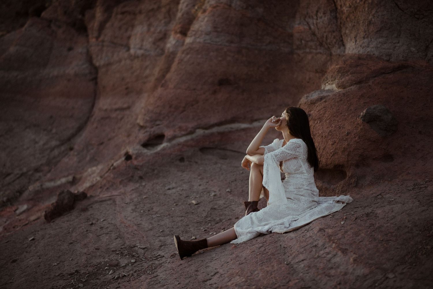 Artistic bridal portrait sitting on red rock formations in white lace.