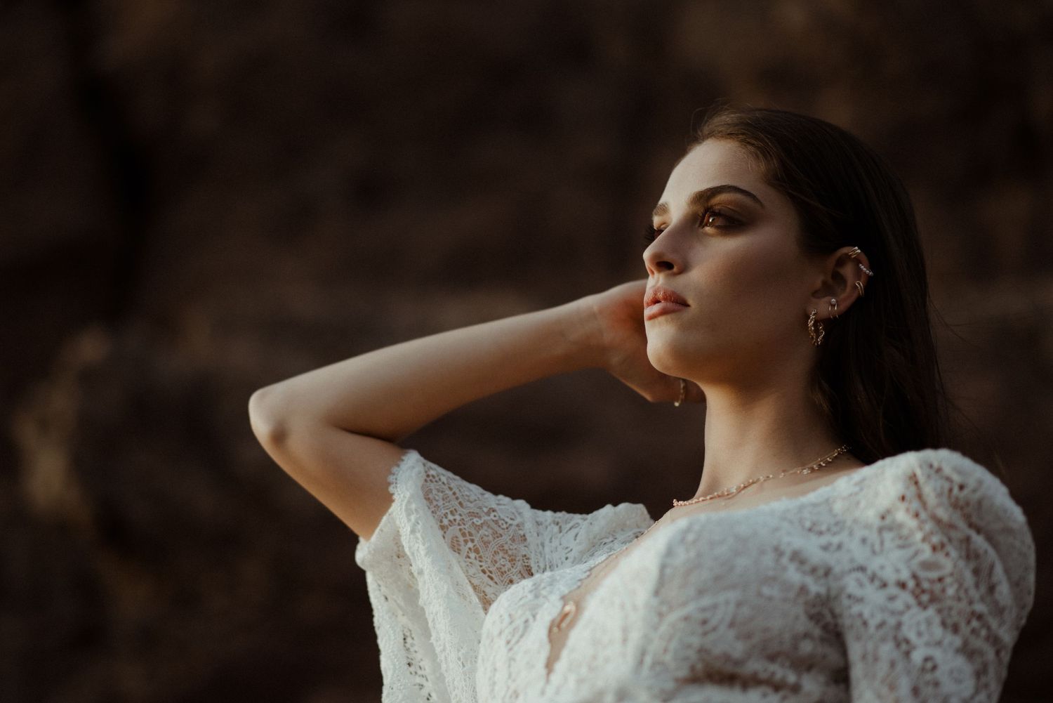 A romantic portrait in a lacy white dress against a dramatic dark background at sunset.