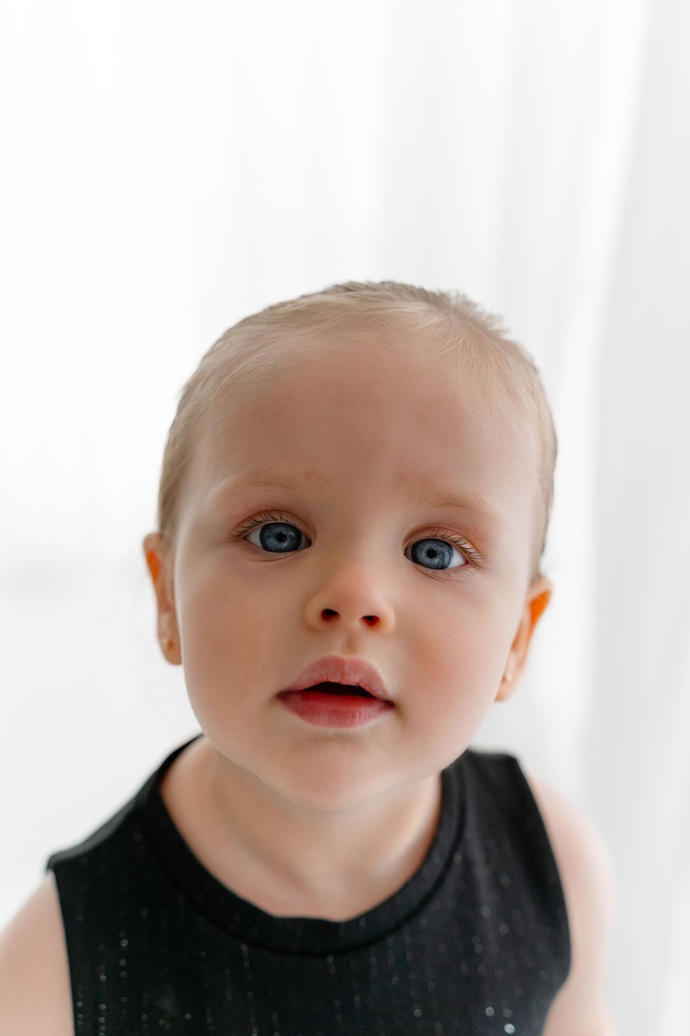 Close up portrait of a small child with bright blue eyes wearing a black tank top against a white background.