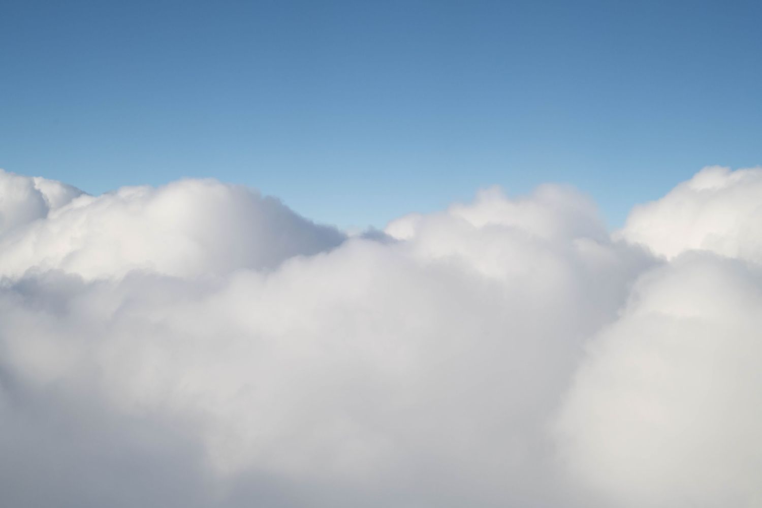 Aerial view of billowing white cumulus clouds stretching across a clear blue sky.