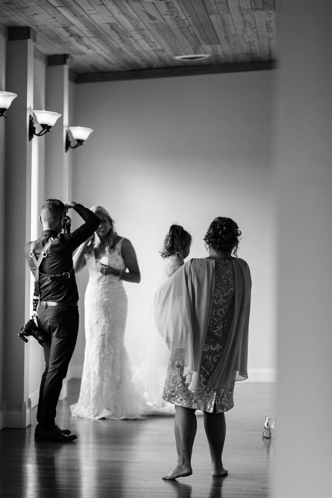 A candid black and white moment of a wedding photographer capturing the bride with guests.