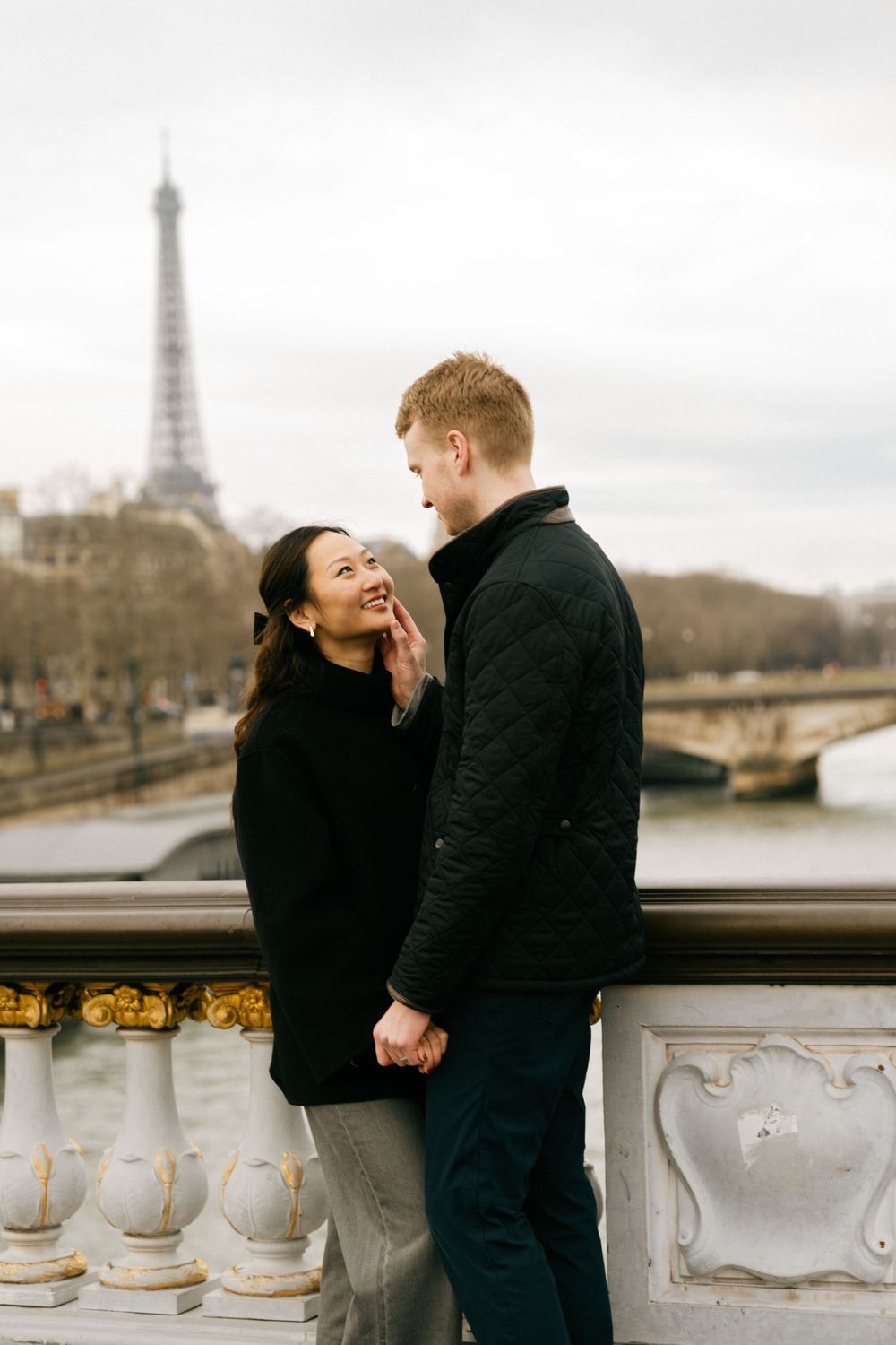 A couple shares a romantic moment together with the Eiffel Tower visible in the background on a cloudy Paris day.