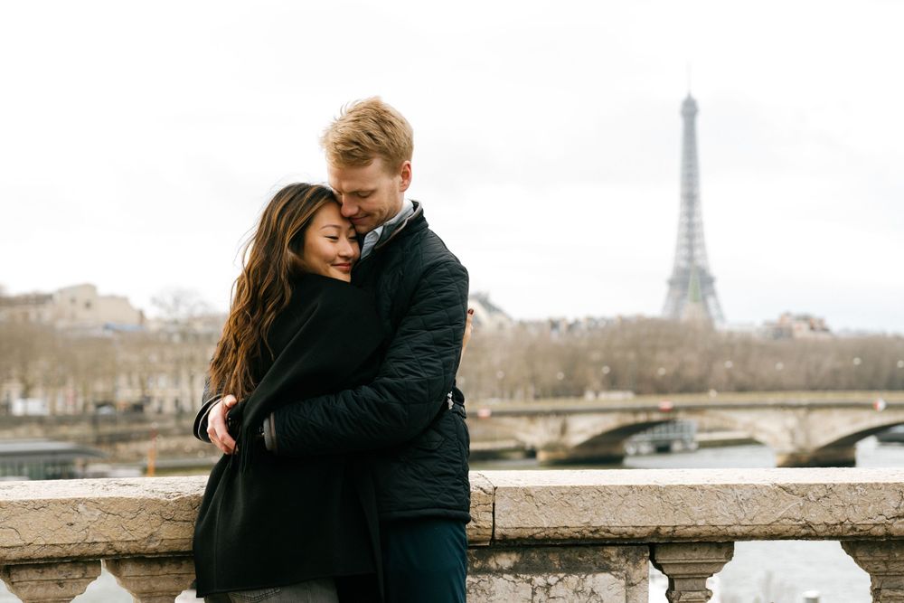 A couple shares an intimate embrace along the Seine River with the iconic Eiffel Tower visible in the background in Paris.