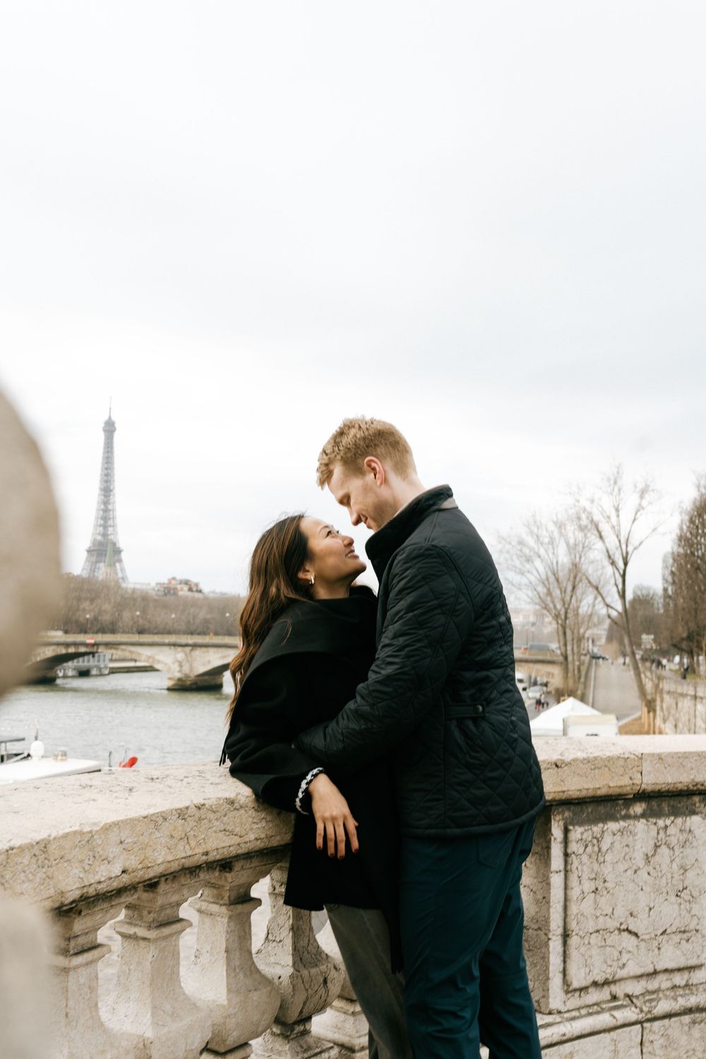 A romantic moment between a couple on a bridge in Paris with the Eiffel Tower visible in the background.