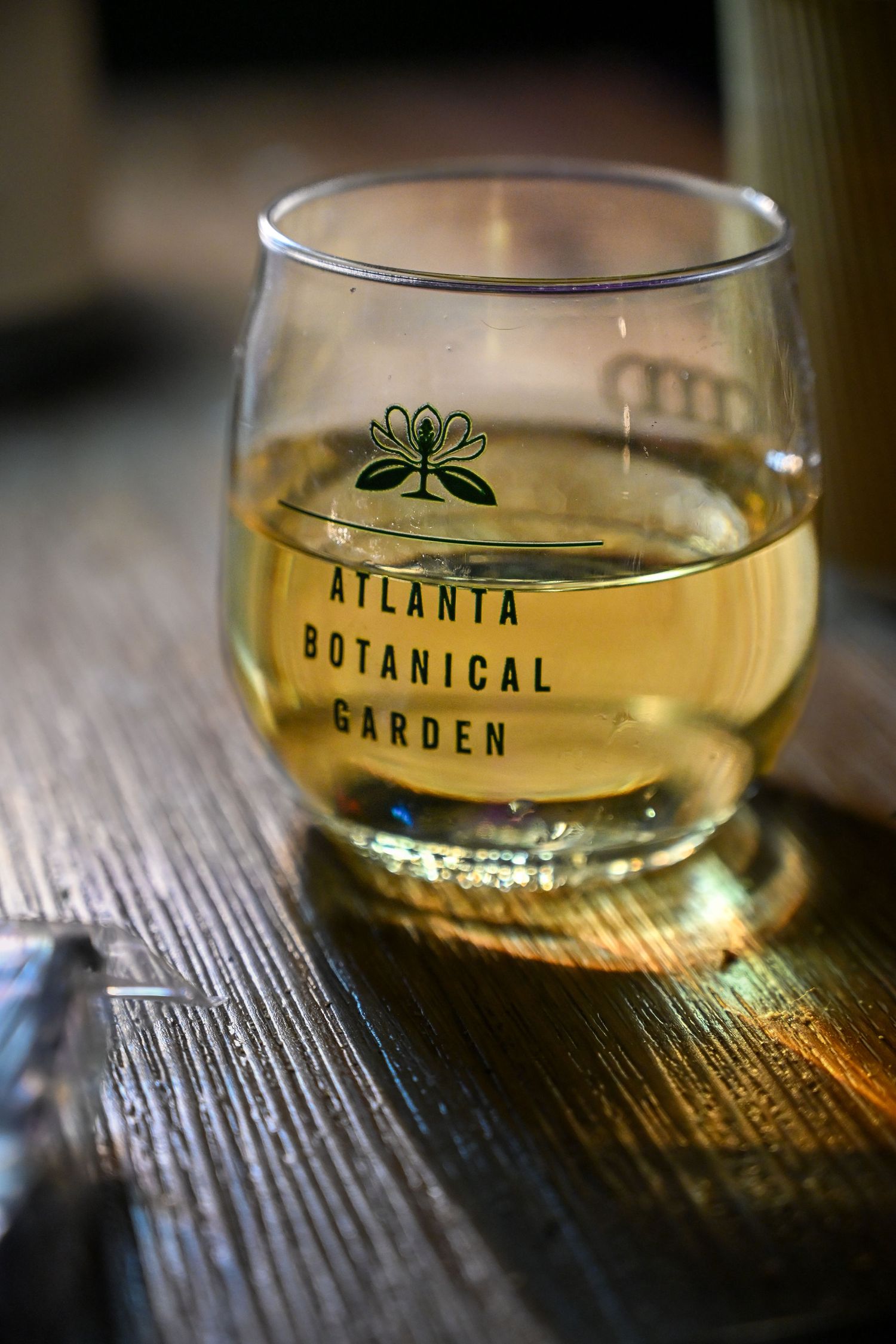 Glass of golden beverage with Atlanta Botanical Garden logo on wooden table.