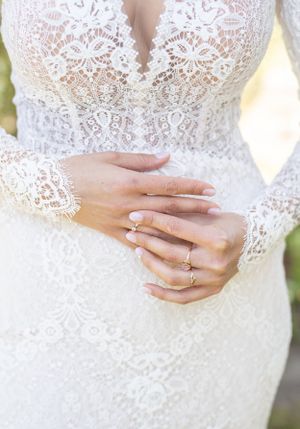 Close up of hands wearing engagement ring and wedding band with lace sleeve detail.
