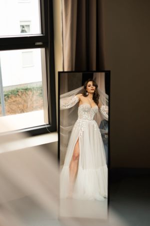 Wedding dress reflection in full-length mirror by window with natural light.