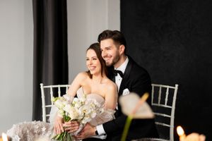 Romantic wedding reception scene with couple at white Chiavari chairs and floral centerpiece.