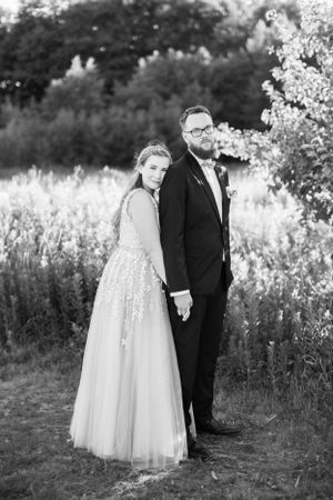 Elegant black and white wedding portrait of couple standing in a wildflower field at dusk.