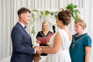 Wedding ceremony taking place under a floral arch with couple exchanging vows before an officiant.