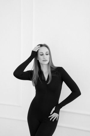 Person in black outfit striking dramatic pose against white wall.