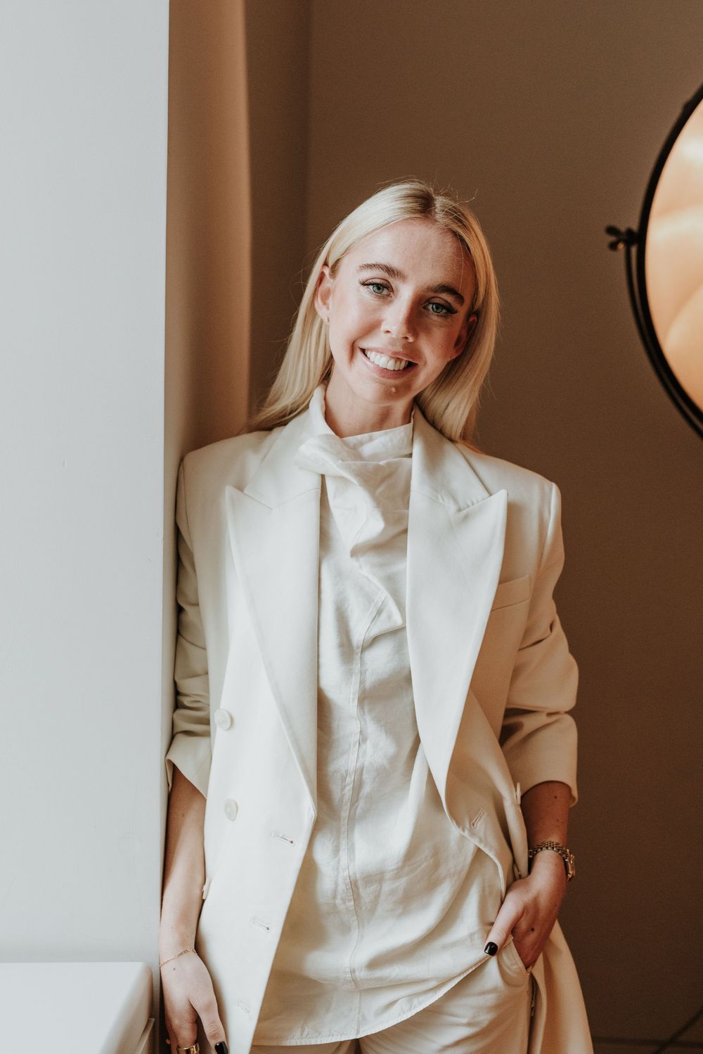 Professional portrait of someone wearing a stylish cream colored blazer and blouse in a minimalist indoor setting.