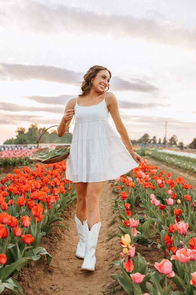 A woman in a white dress walks through vibrant red tulip fields at sunset.