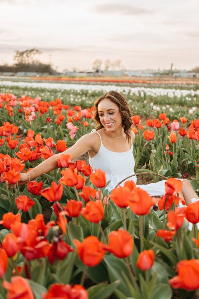 Figure in white dress dancing among rows of bright orange tulips in a flower field.