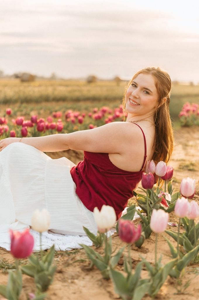 Woman in burgundy dress poses gracefully among blooming pink tulip fields at sunset.