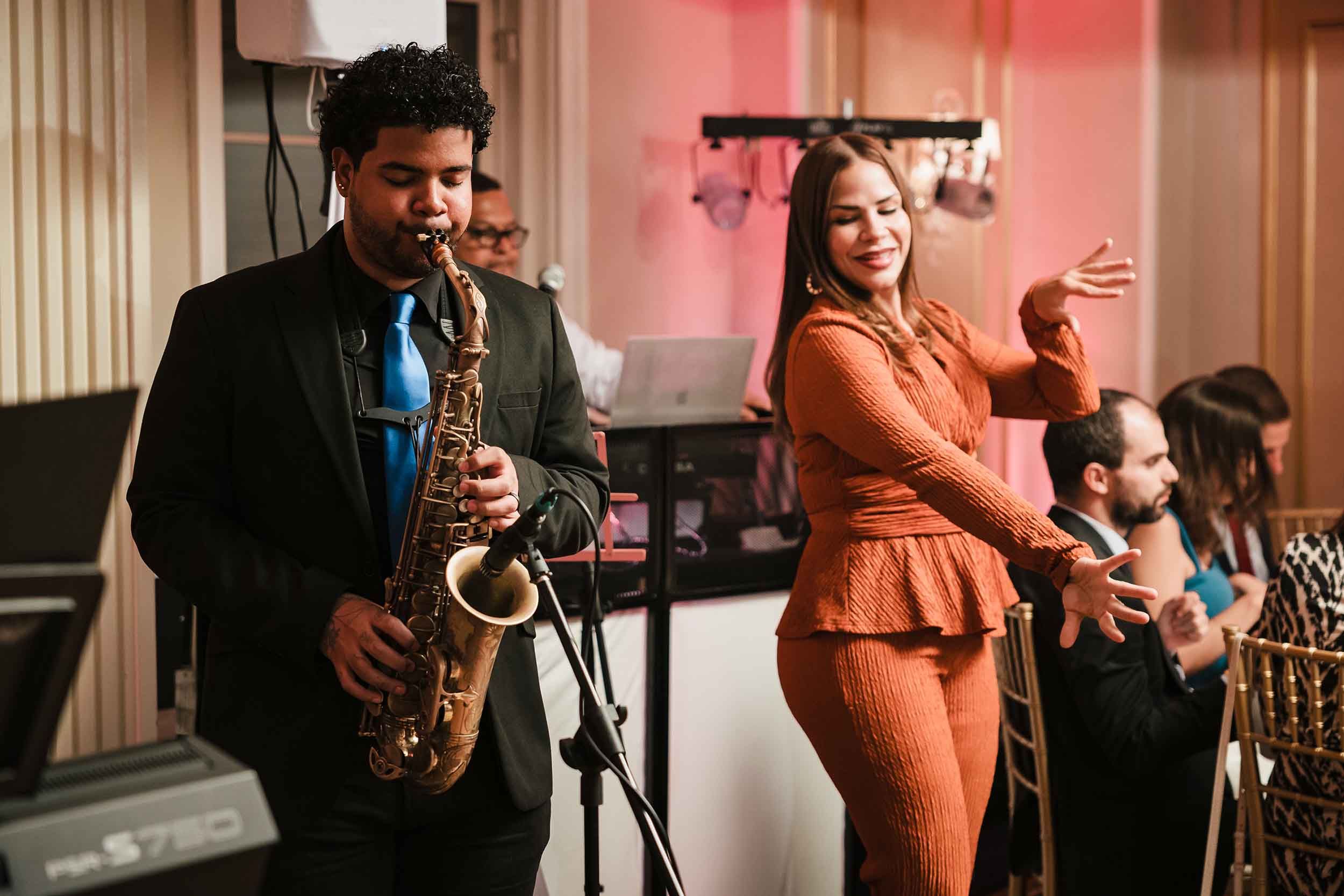 Saxophonist playing alongside a singer dancing during a Grupo Chevere live performance at a Lenox Hotel Boston wedding reception.