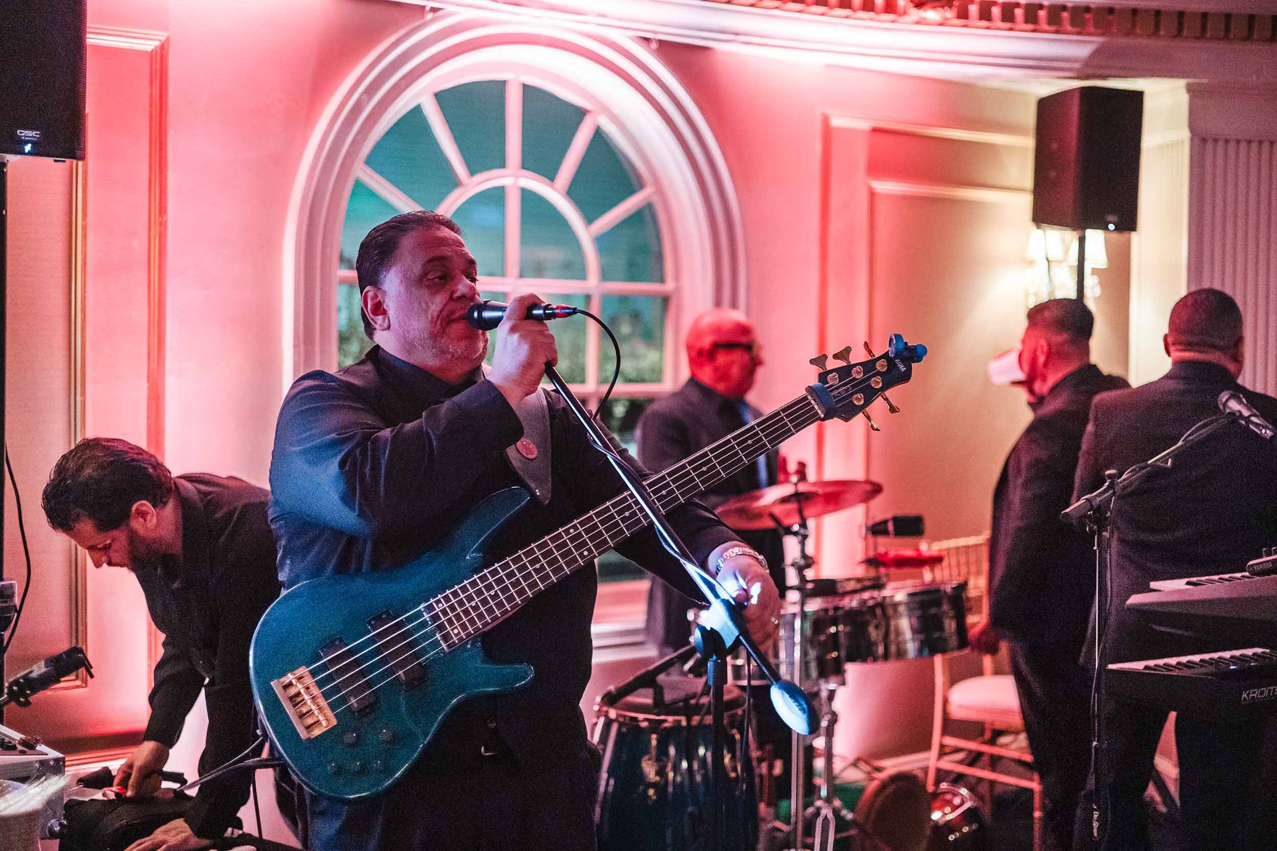 Bassist singing into a microphone during a Grupo Chevere live band performance at a wedding reception in Boston.