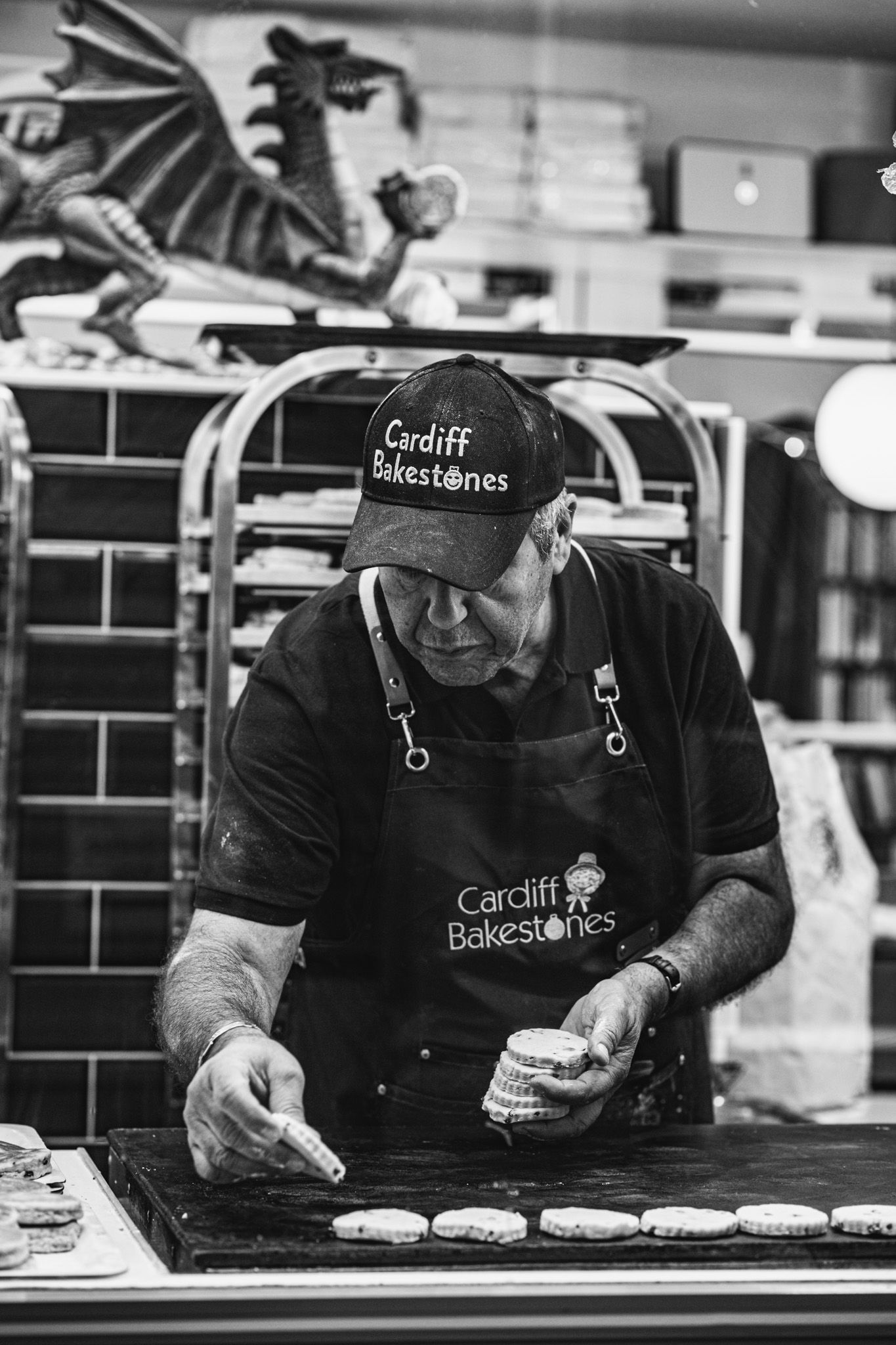 Black and white photo of a baker decorating pastries at Cardiff Bakestones market stall.