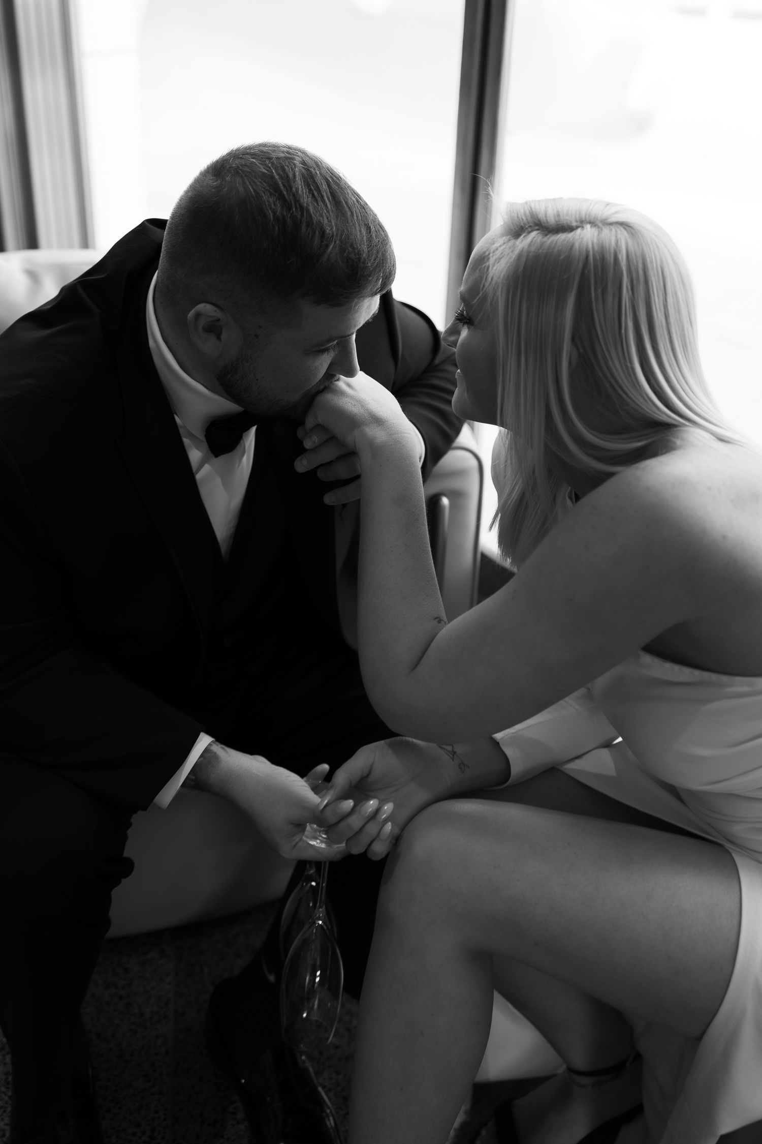 Couple in Bottleworks Hotel lobby, guy kissing her hand, holding wine glasses, look at each other, Indianapolis engagement session