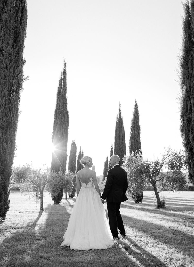 Wedding couple walking through château gardens in France surrounded by cypress trees  warm evening light in a romantic destination setting