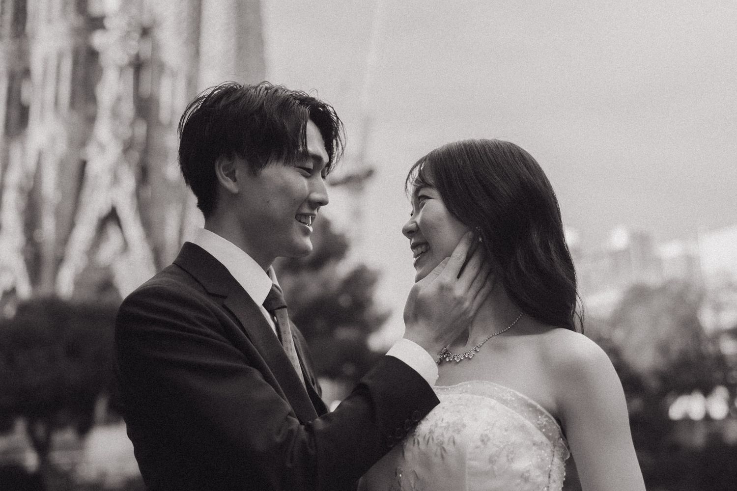 A couple in wedding attire embraces in front of the iconic Sagrada Familia cathedral in Barcelona, Spain.