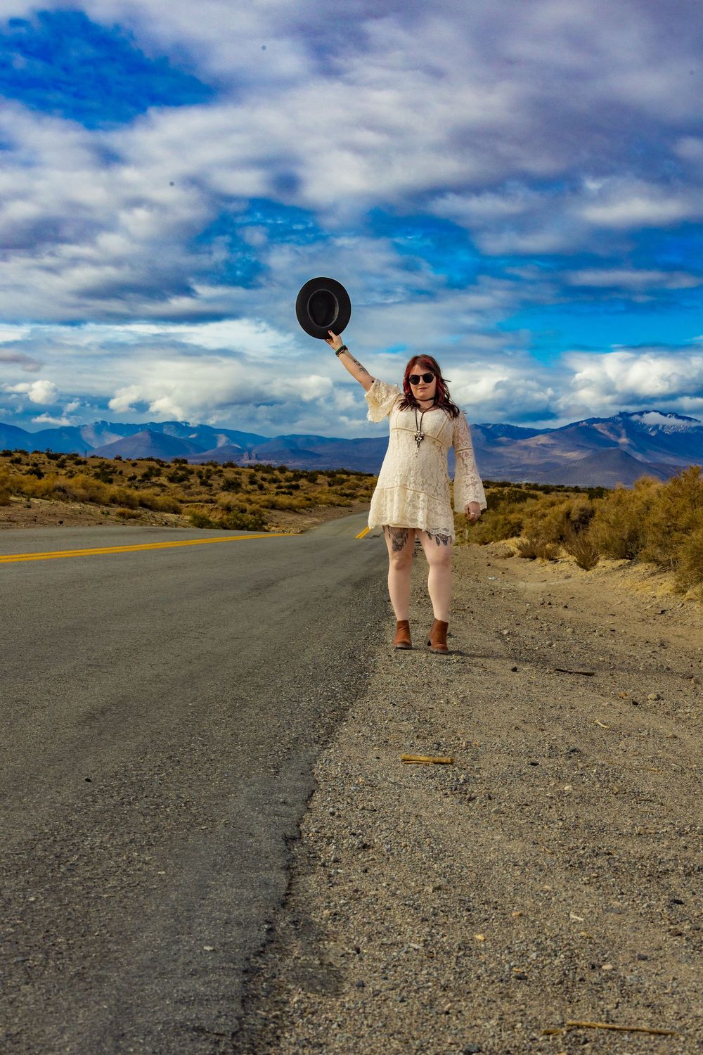 Woman in white lace dress on desert road with mountains and blue sky by Zeus Holbrook Wedding Photographer
