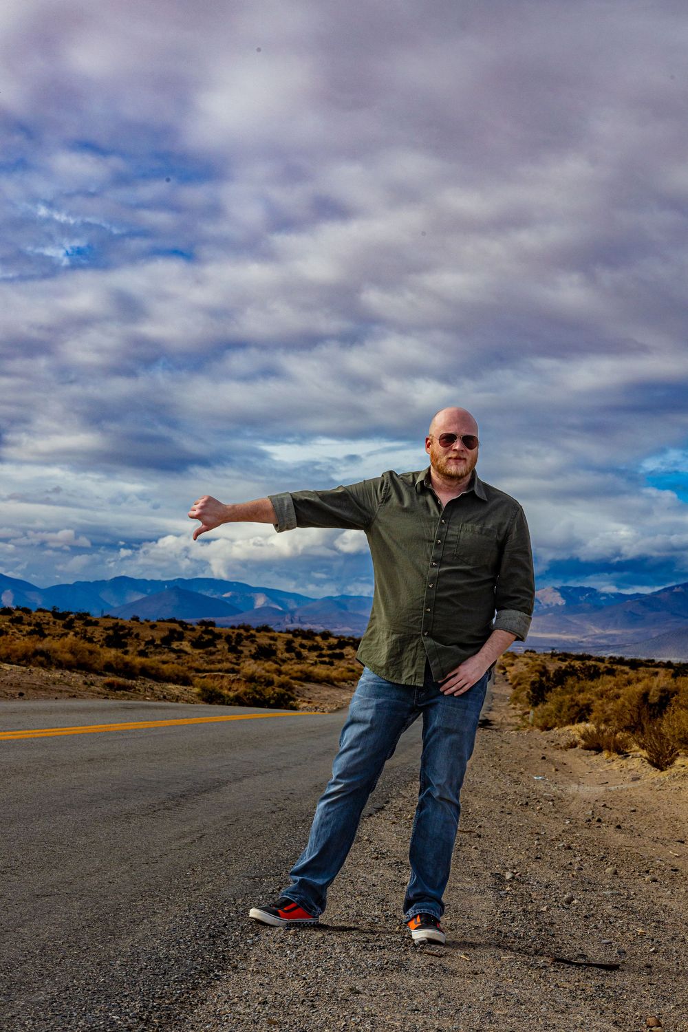 Person on a desert road with outstretched arm against dramatic cloudy sky by Zeus Holbrook Wedding Photographer