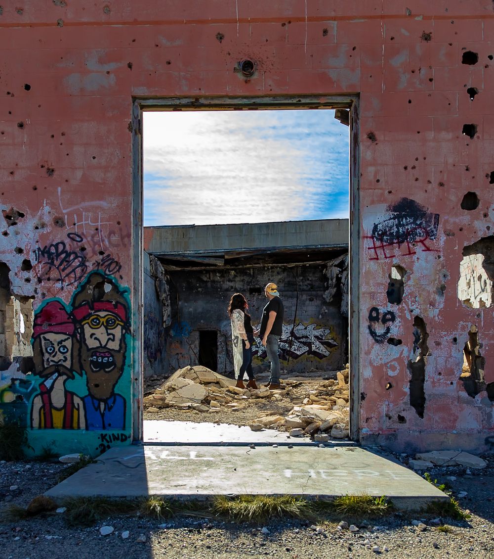 Abandoned pink concrete building with graffiti art and broken windows in a desert landscape.
