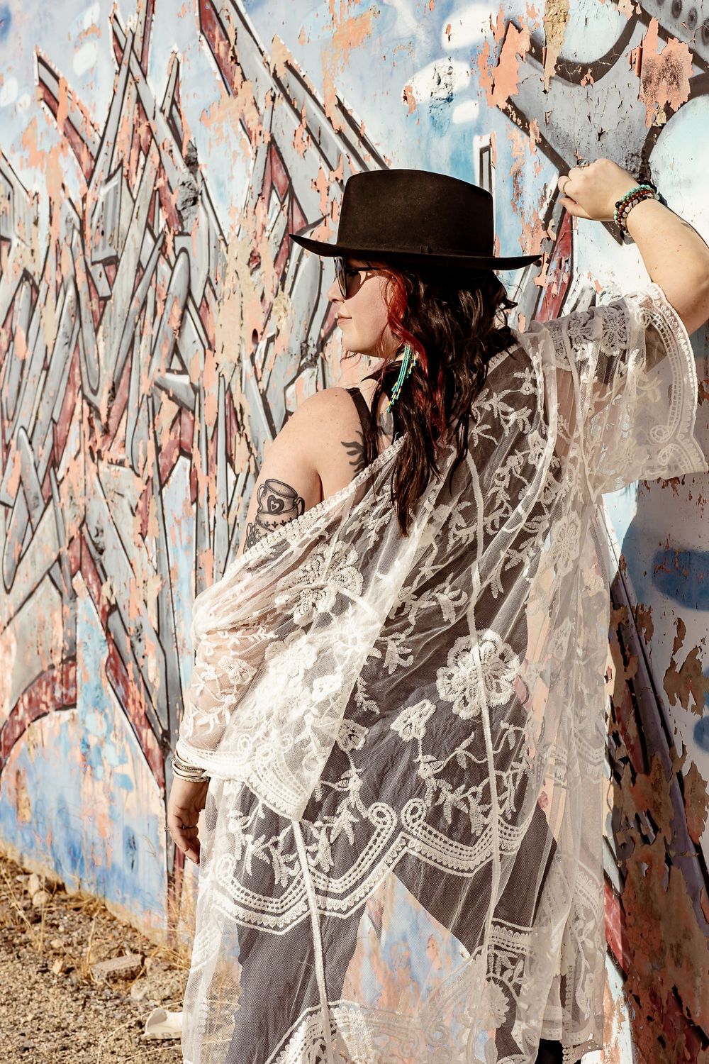 A series of photos showing a person in a black hat and white lace dress posing against a painted wall background.