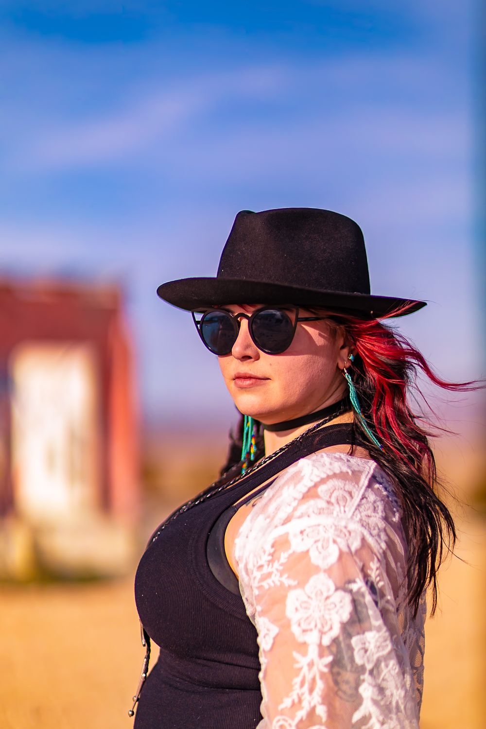 Person wearing a black hat and white lace dress against a blue sky and desert backdrop.
