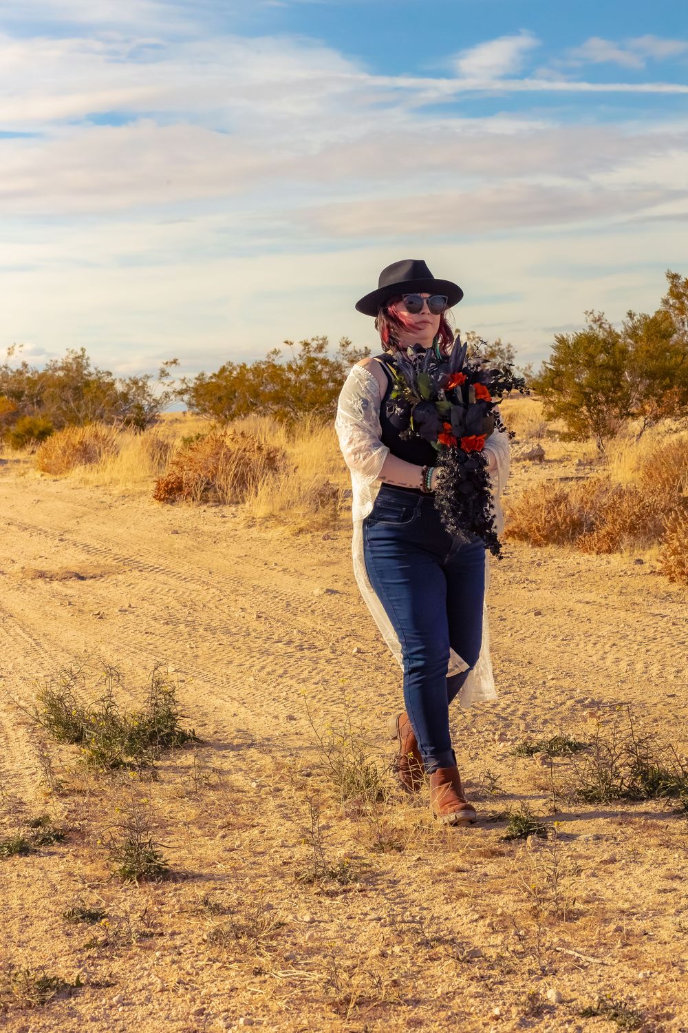 A photographer wearing a black hat and jeans crouches to capture shots in a desert landscape during golden hour.