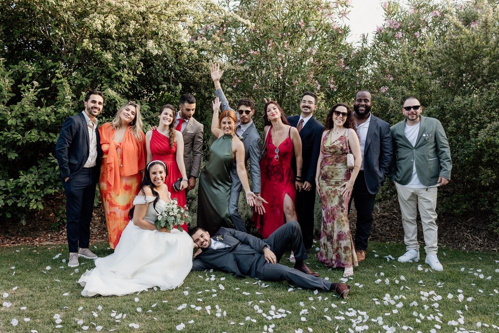 A group poses together on a lawn with white flowers scattered on the grass during a festive outdoor celebration.