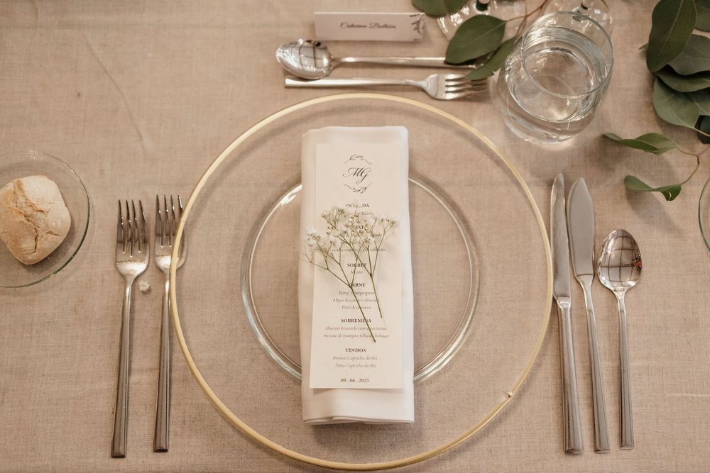 Elegant table setting with white plates, silverware, wine glasses and napkins arranged on a beige tablecloth.