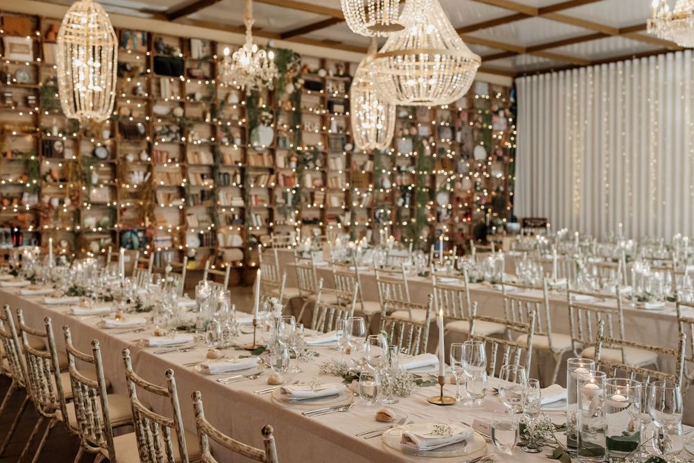 Elegant wedding reception venue with crystal chandeliers, white table settings, and floral centerpieces in a modern space.